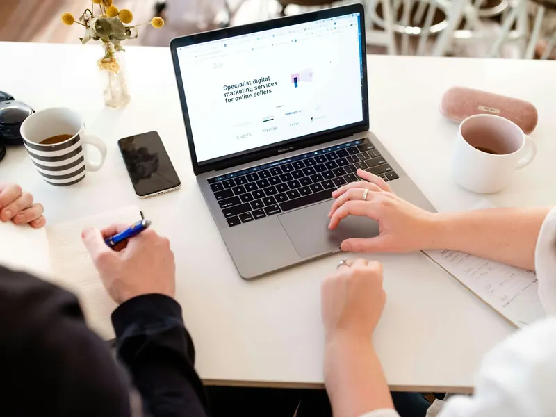 Zwei Personen besprechen sich an einem Tisch mit Laptop und Notizen